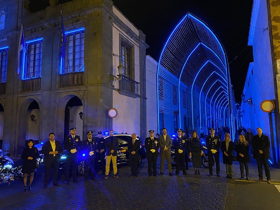 Agentes de la Policía Nacional y autoridades posando frente a edificio iluminado de color azul. 